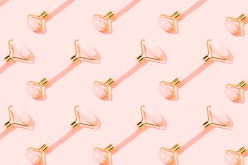Pattern made with pink Gua Sha massage tools. Rose Quartz jade roller on pink background. Anti age, ...