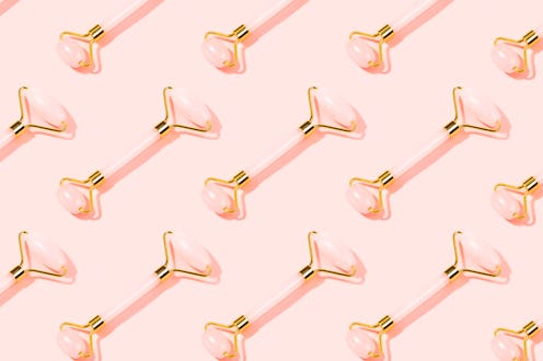 Pattern made with pink Gua Sha massage tools. Rose Quartz jade roller on pink background. Anti age, ...