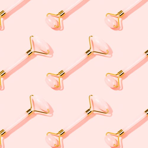 Pattern made with pink Gua Sha massage tools. Rose Quartz jade roller on pink background. Anti age, ...