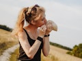 A young woman eats a taco on a sunny day in a grassy field.