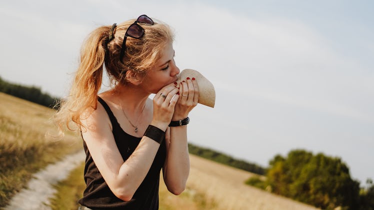 A young woman eats a taco on a sunny day in a grassy field.