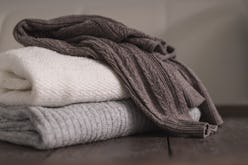 Stack of neatly folded woolen knitwear. Minimal lifestyle, capsule wardrobe. Autumn-winter men fashi...