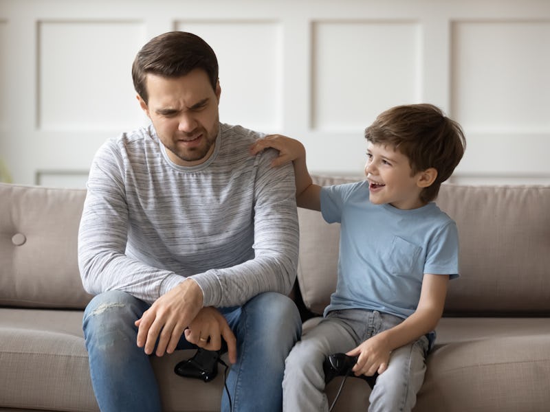 Happy small child boy put hand on fathers shoulder, supporting after losing video game. Excited litt...