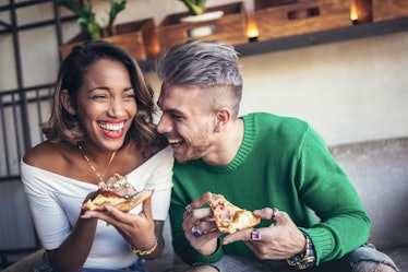 Mixed race couple eating pizza in modern cafe. They are laughing and eating pizza and having a great...