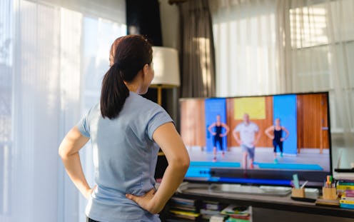 A person stands with their hands on their hips, facing away from the camera to watch three exercise ...