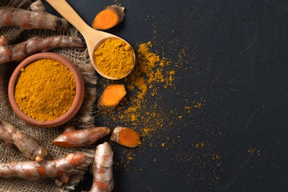 turmeric powder in wood spoon with turmeric root on black table, spices and herb concept