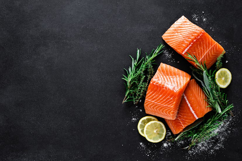 Salmon. Fresh raw salmon fish fillet with cooking ingredients, herbs and lemon on black background, ...