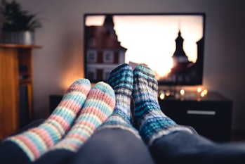 Couple with socks and woolen stockings watching movies or series on tv in winter. Woman and man sitt...