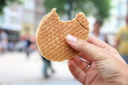 A woman's hand holds up a stroopwafel with a bite taken out of it. 