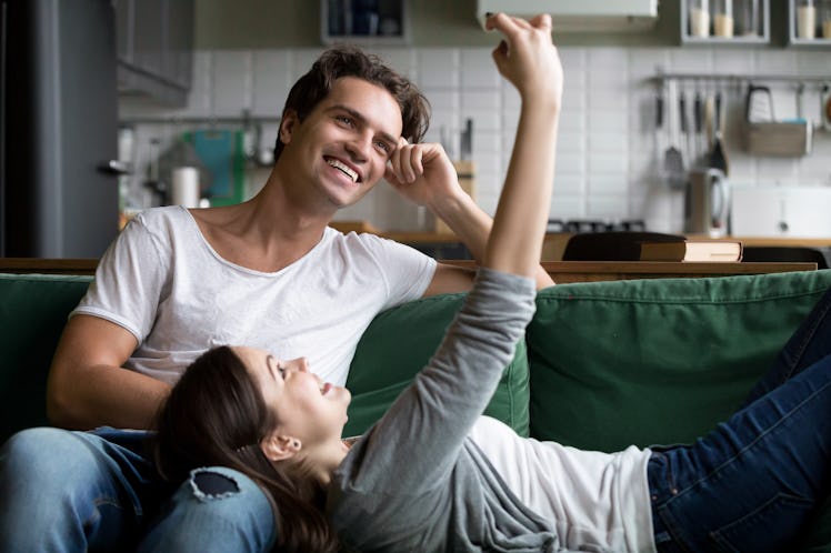 A happy couple smiles for the camera while lounging on the couch at home.