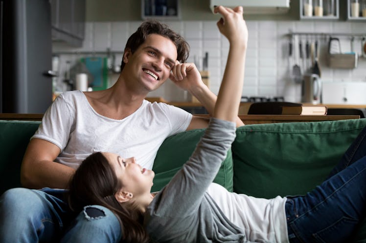 A happy couple smiles for the camera while lounging on the couch at home. 