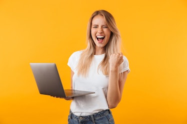 Portrait of an excited young blonde girl holding laptop computer and celebrating success isolated ov...
