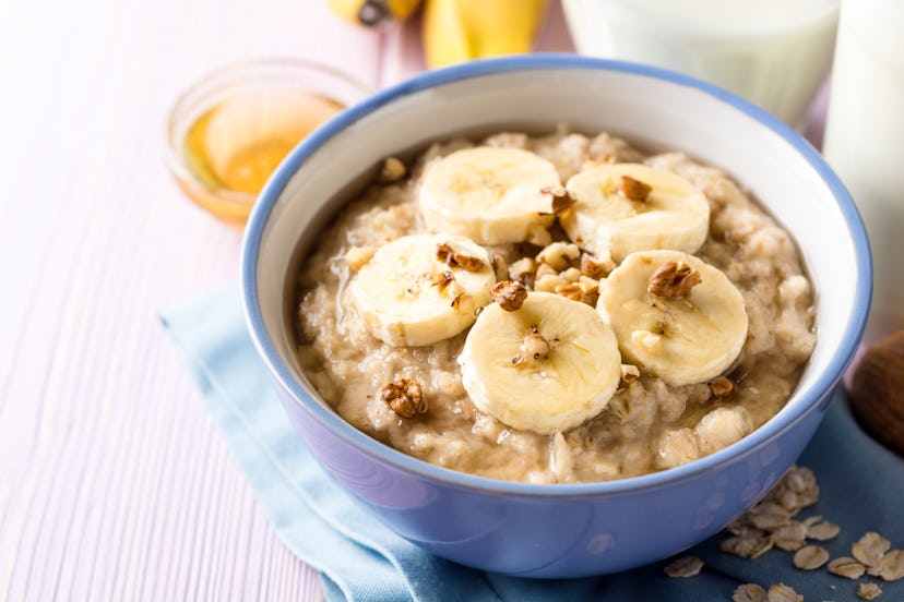 Oatmeal porridge with banana, walnuts and honey in bowl on purple wooden background. Healthy breakfa...