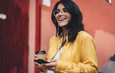 Happy girl in hipster eyeglasses listening to music while going to work, cheerful hispanic woman dri...