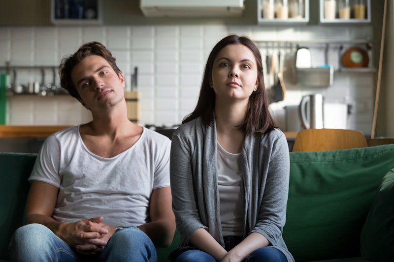 Lazy millennial couple getting bored at home sitting on sofa, young funny disinterested girl and guy...