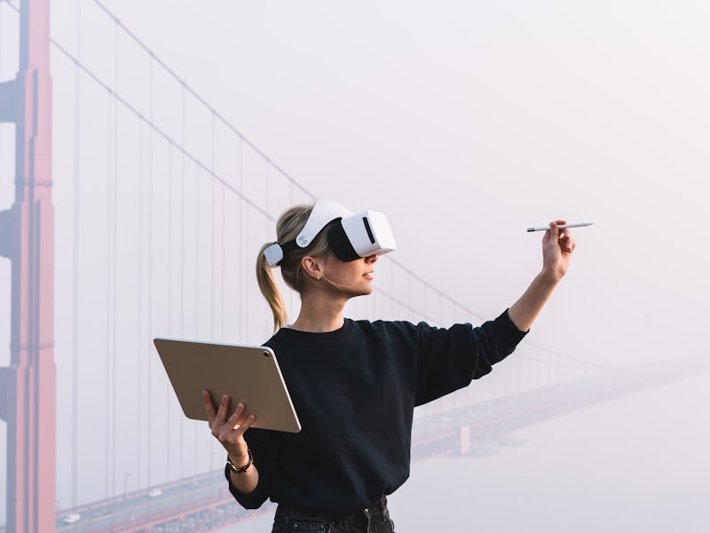 Young female extend hand with digital pencil for interactive touch over air while standing in agains...