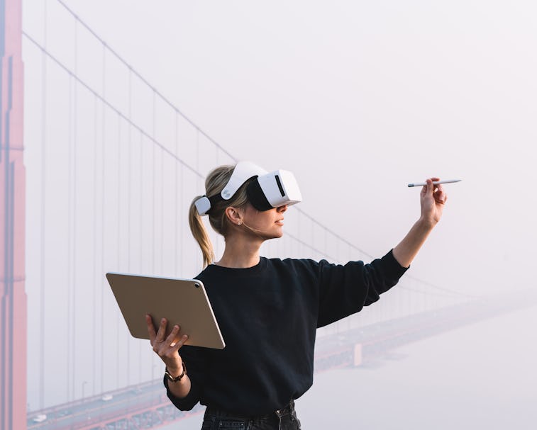 Young female extend hand with digital pencil for interactive touch over air while standing in agains...
