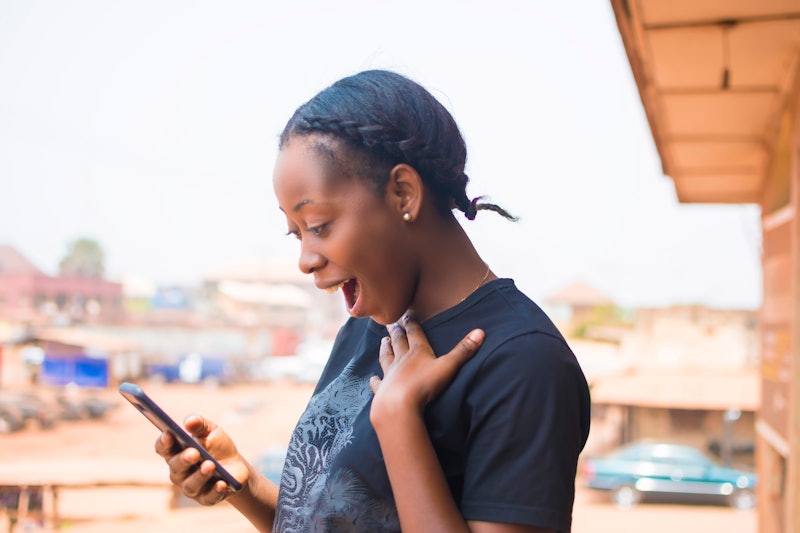 young African lady browsing with her mobile phone with surprised on her face