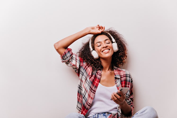 Gorgeous african girl holding smartphone and listening music. Fascinating female model enjoying song...