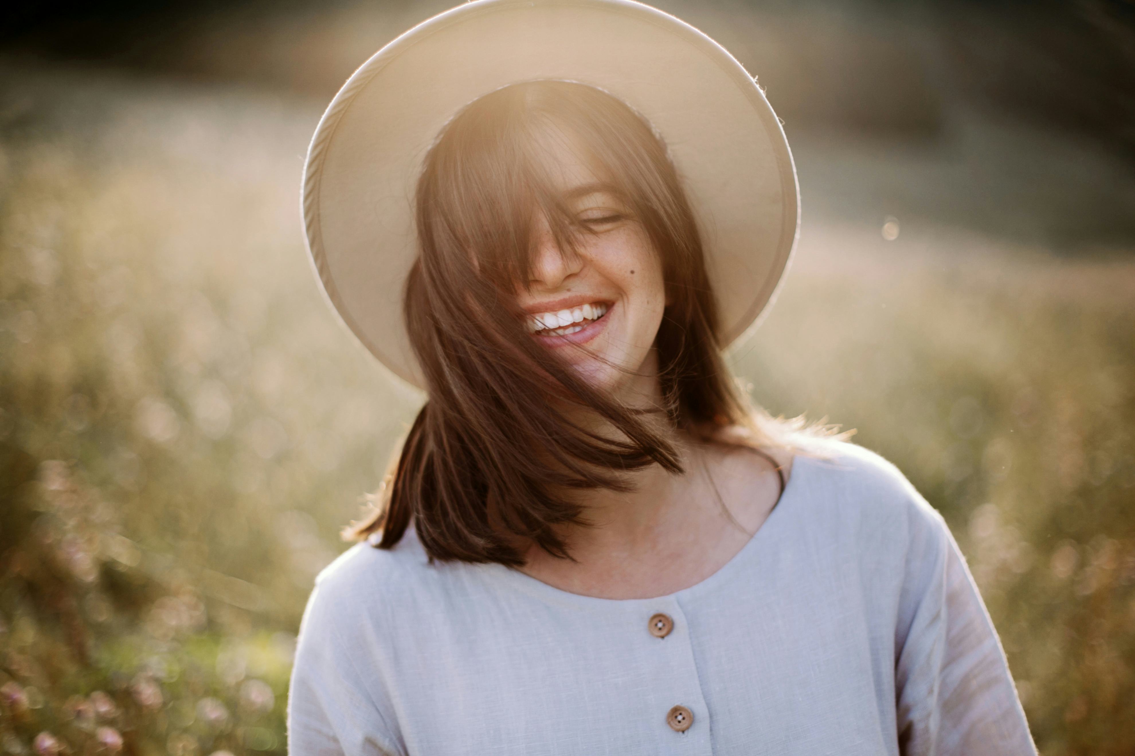Stylish girl in rustic dress smiling and waving hair in sunny meadow in mountains. Portrait of happy...