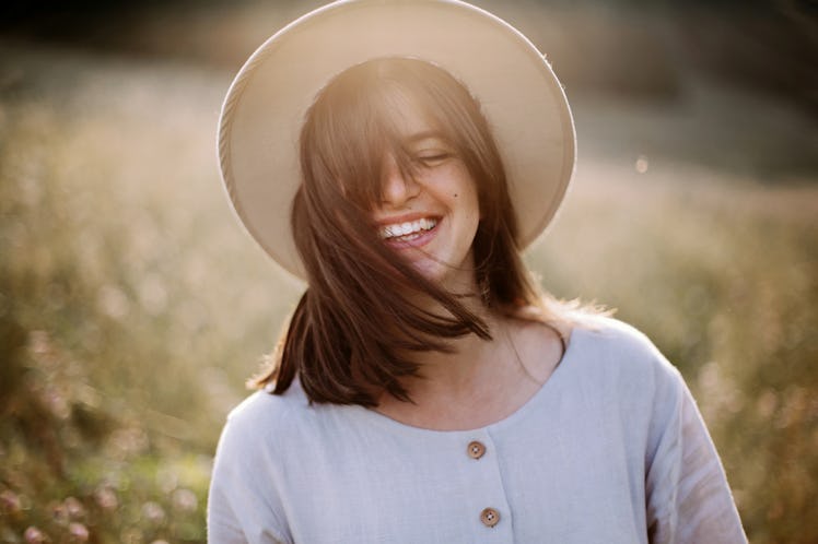 Stylish girl in rustic dress smiling and waving hair in sunny meadow in mountains. Portrait of happy...