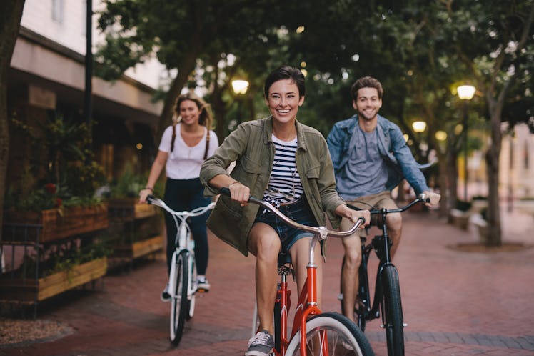 Three happy best friends ride bicycles down a street. 