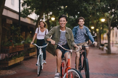Three happy best friends ride bicycles down a street. 
