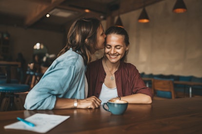 Happy young woman kissing her girlfriend, sitting in a cafe. Happy lesbian couple in love.