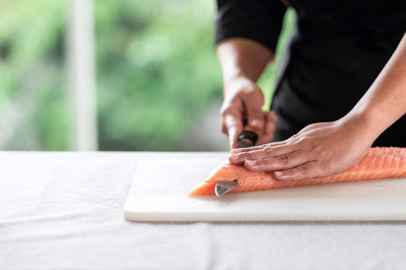 Chef slicing raw salmon on plastic plate. Asian woman chef in black uniform, start to slice.