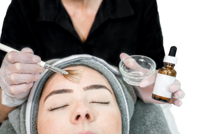 Cosmetologists applying chemical peel treatment on a patient in a beauty spa.