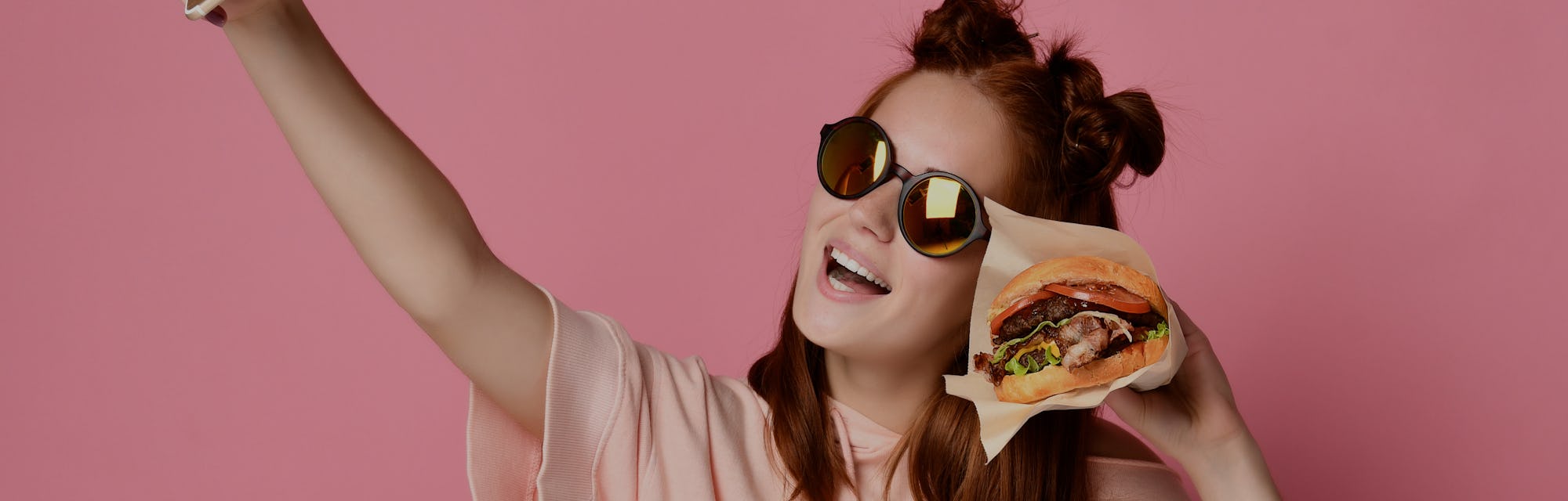 Positive ginger young woman pose for selfie, use modern cell phone, sit with burger in hand , have f...