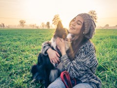 Young beautiful girl stroking her dog in a park at sunset - Asian woman playing with her dog