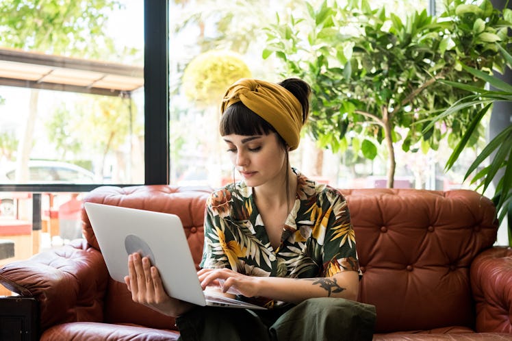 Pretty brunette girl checks her mail on small portable laptop while waiting her order in cafe shop. ...