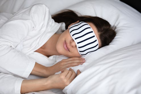 Calm serene young woman wear pajamas and sleeping mask resting in comfortable white bed, peaceful he...