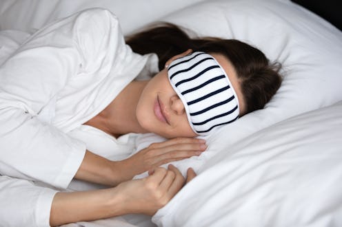 Calm serene young woman wear pajamas and sleeping mask resting in comfortable white bed, peaceful he...