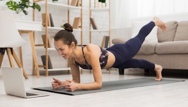 Fit woman doing yoga plank and watching online tutorials on laptop, training in living room