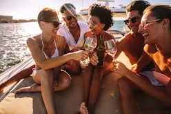 A group of friends laugh and toast their wine glasses on a boat at sunset.