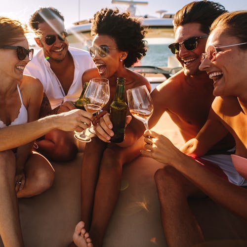 A group of friends laugh and toast their wine glasses on a boat at sunset.