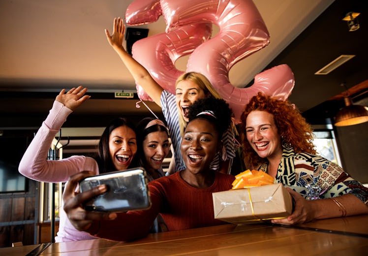 A group of friends all smile for a birthday selfie with a balloons and a present.