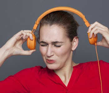 tinnitus headphones concept - stressed out 20s girl listening to loud music with earphones on,removi...