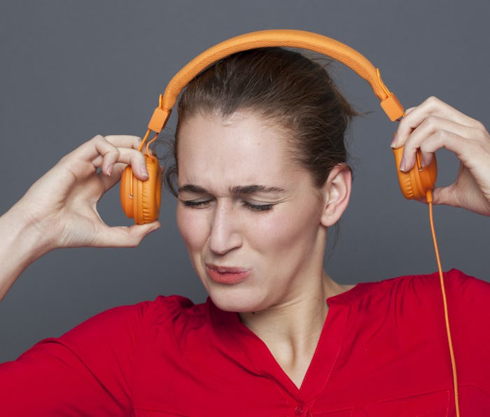 tinnitus headphones concept - stressed out 20s girl listening to loud music with earphones on,removi...