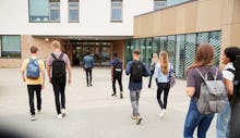 Rear View Of High School Students Walking Into College Building Together