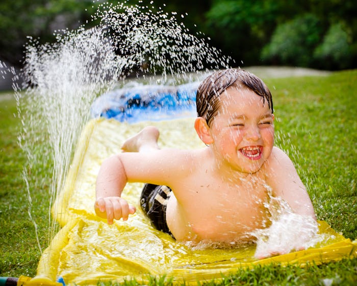 Happy child on water slide to cool off on hot day during spring or summer