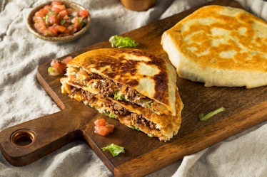 A homemade beef Crunchwrap Supreme like at Taco Bell, sits on a cutting board with lettuce and tomat...