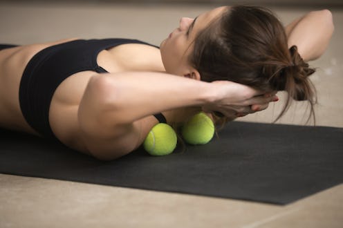 Lifestyle shot of young attractive female practicing self-massage technique applying tennis balls fo...