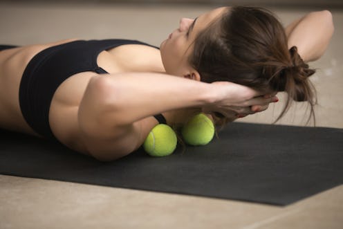 Lifestyle shot of young attractive female practicing self-massage technique applying tennis balls fo...
