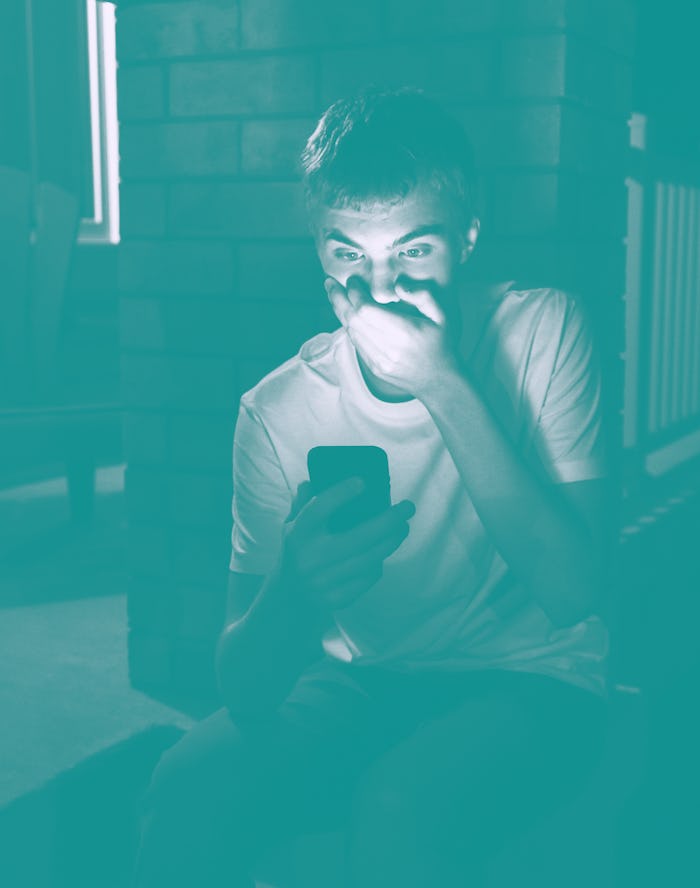 Teenager looking at something shocking on his mobile phone. He is sitting in front of his house at n...