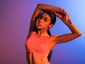 attractive sportive african american girl in pink sports bra posing on purple and blue gradient back...