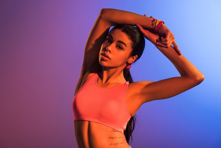 attractive sportive african american girl in pink sports bra posing on purple and blue gradient back...