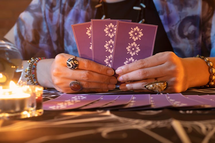 Tarot reader or Fortune teller of hands holding up purple deck tarot cards.Tarot cards spread on tab...